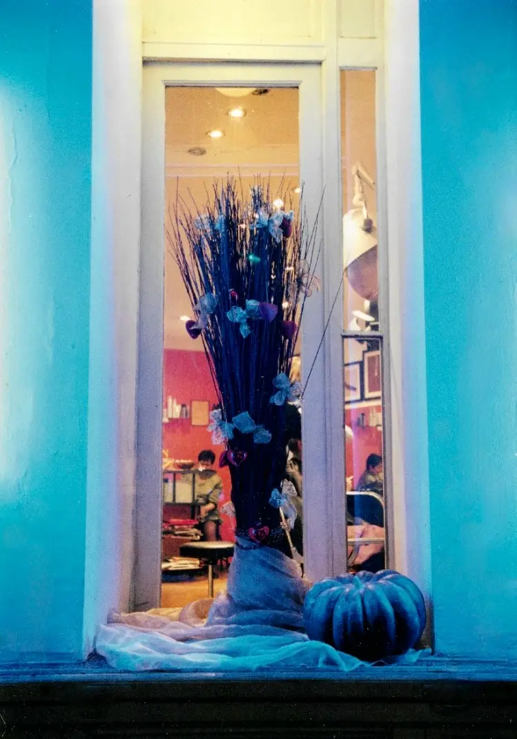 Blick von außen durch das Schaufenster der HAIR-FACTORY — blaue Dekoration mit Zweigen und einem Kürbis, warmes Licht aus dem Salon.